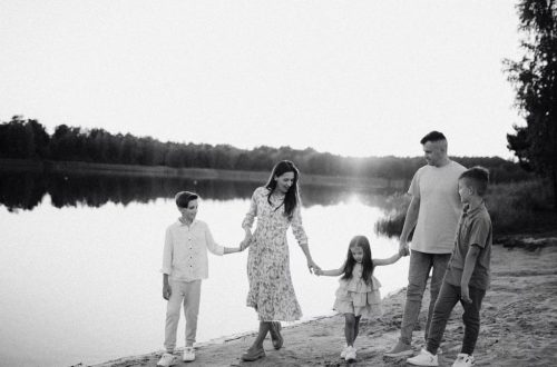 Monochrome photo of a family walking hand in hand along a serene lakeshore.