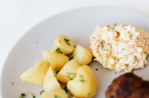 From above of plate with juicy fried meat cutlet served with delicious Russian meat salad and boiled potatoes topped with parsley placed on white table