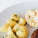 From above of plate with juicy fried meat cutlet served with delicious Russian meat salad and boiled potatoes topped with parsley placed on white table